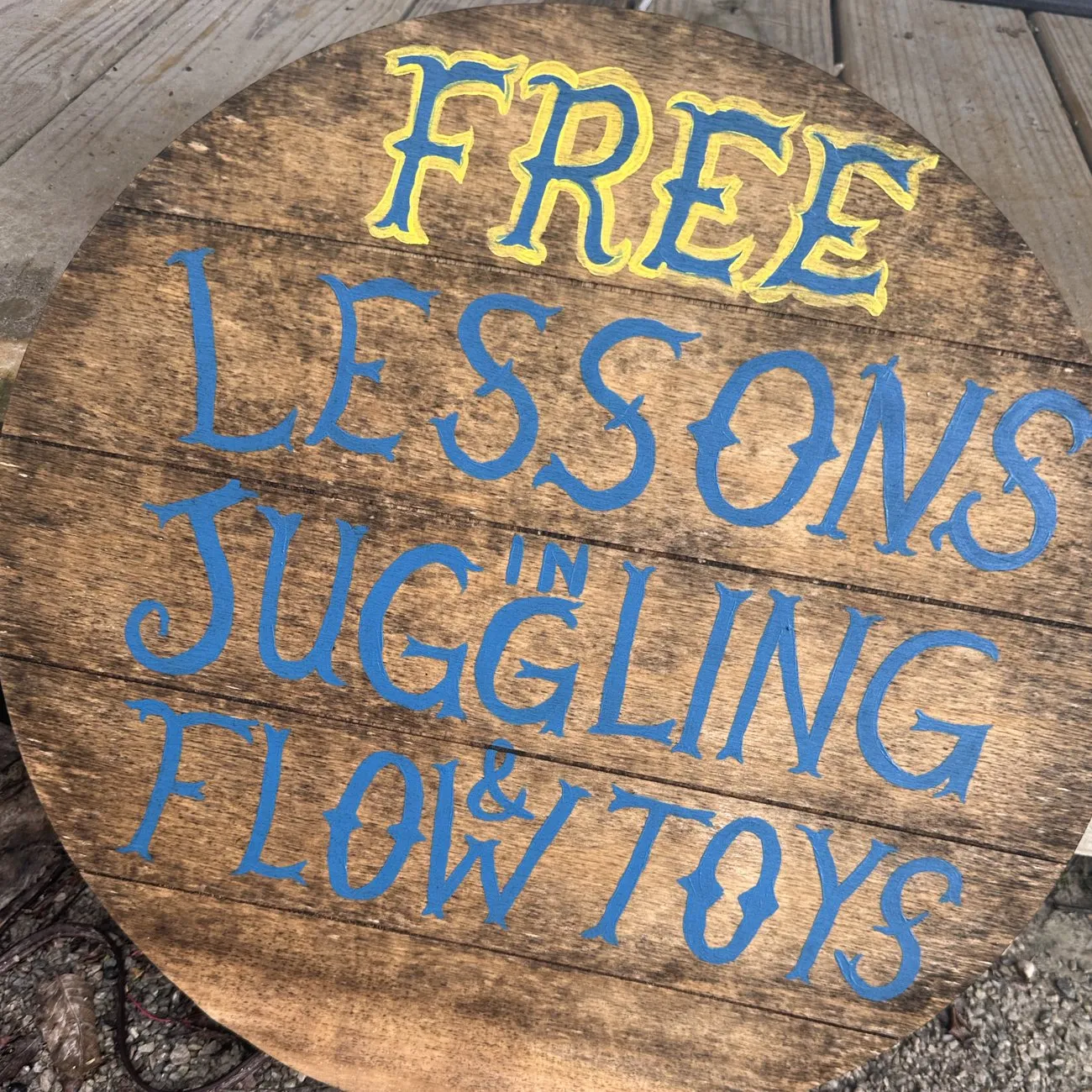 Round hand-painted wooden sign reading "Free lessons in juggling & flow toys"