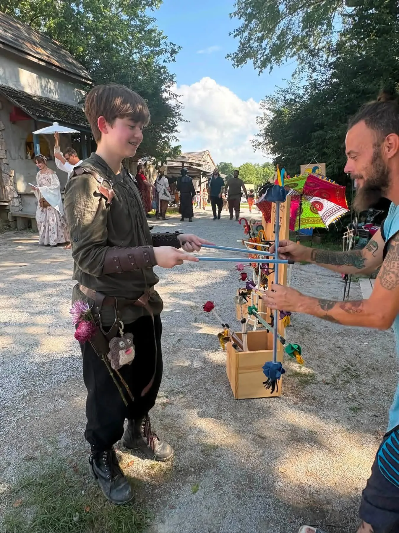 A young festival-goer learning Jester Stix outside the booth, sticks mid-pass