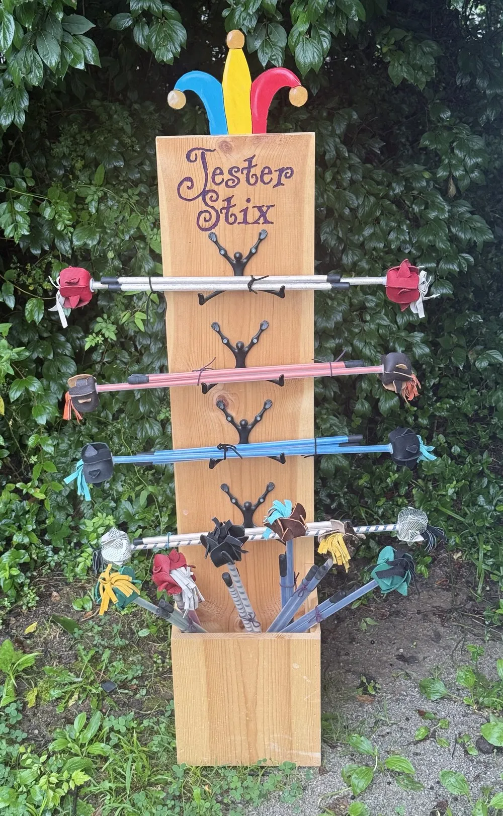 The Jester Stix display stand at the booth: rows of sticks tipped with colorful hand-cut leather flower ends, under a carved jester-hat topper
