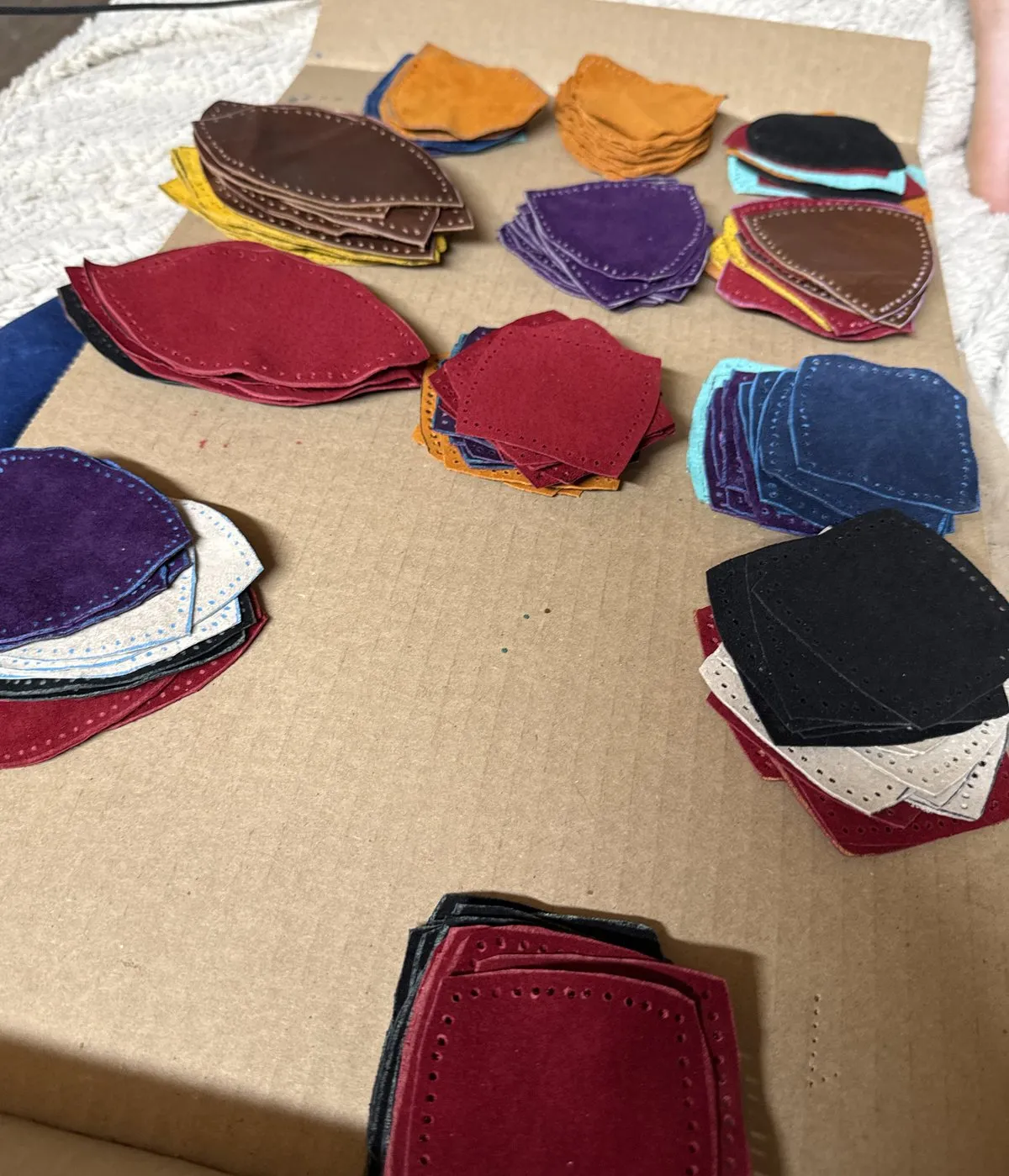 Stacks of hand-cut leather panels and flower-end petals in many colors on the workbench